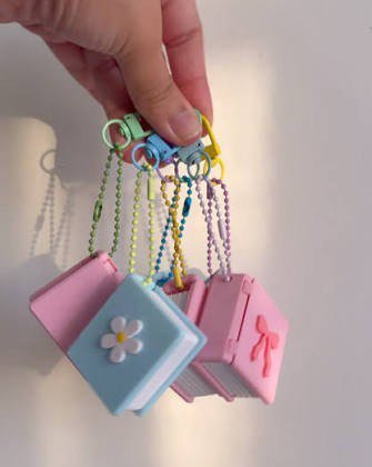 A hand holding several pastel mini book keychains